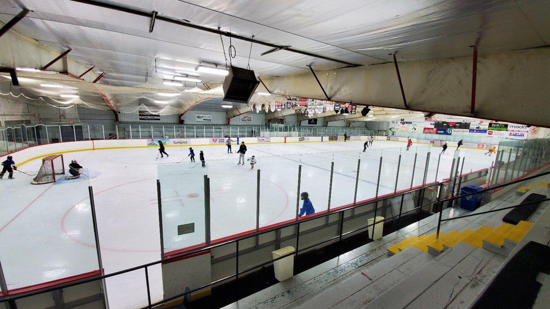 A wide shot of an ice rink set up for a hockey game. There are a few players on the ice. 