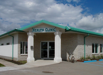 Front view of the Carberry Health Clinic, a low stone building with two white front columns and a green roof. 